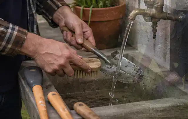 Hände reinigen gebrauchte Gartengeräte mit Bürste und Wasser am Außenbecken; Thema Husqvarna Automower, Schwerpunkt Sicherheit; Ausgangslage.