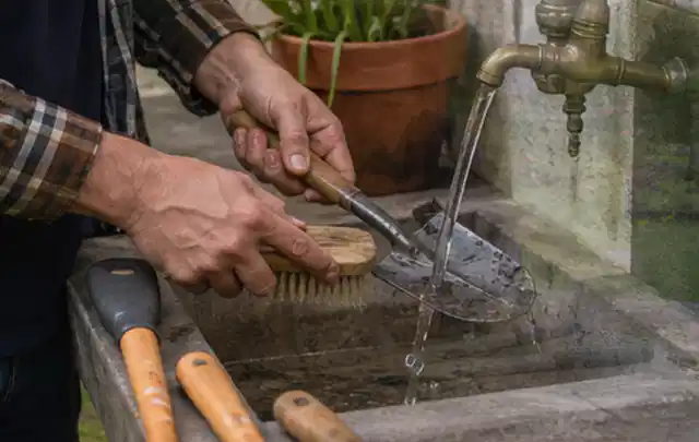 Hände reinigen gebrauchte Gartengeräte mit Bürste und Wasser am Außenbecken; Thema Husqvarna Automower, Schwerpunkt Systemvergleich; Ausgangslage.