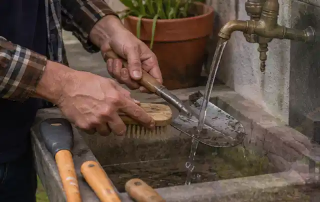 Hände reinigen gebrauchte Gartengeräte mit Bürste und Wasser am Außenbecken; Thema Husqvarna Automower, Schwerpunkt Testkriterien; Umsetzung.