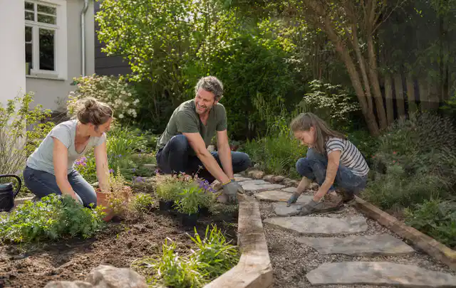 Familie geht auf einem Weg durch einen abwechslungsreich gestalteten Garten; Thema Insektenfreundlicher Garten, Schwerpunkt Wegeführung; Praxisalltag.