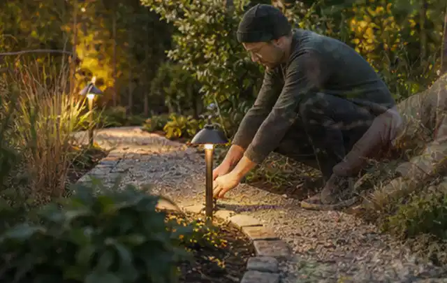 Person richtet eine niedrige warm leuchtende Gartenlampe am Kiesweg aus; Thema Japanischer Garten, Schwerpunkt Garten gestalten; Ergebnis.