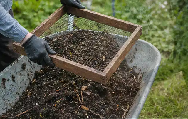 Behandschuhte Hände sieben reifen Kompost über einer Gartenschubkarre; Thema Kiwi, Schwerpunkt Einsteigerwissen; Ausgangslage.