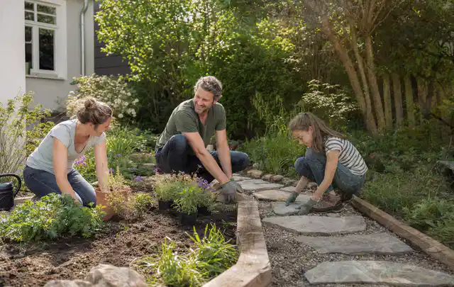 Familie geht auf einem Weg durch einen abwechslungsreich gestalteten Garten; Thema Kleingarten, Schwerpunkt Bepflanzung; Kontrolle.