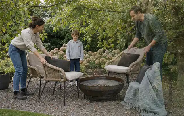 Familie stellt wetterfeste Sessel an einem geschützten Sitzplatz im Garten auf; Thema Kleingarten, Schwerpunkt Privatsphäre; Kontrolle.