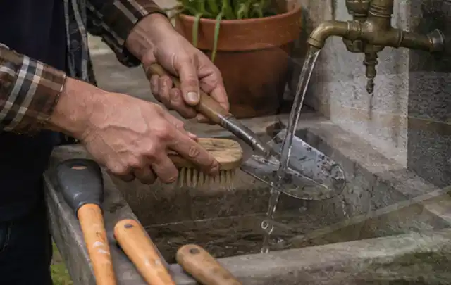 Hände reinigen gebrauchte Gartengeräte mit Bürste und Wasser am Außenbecken; Thema Komposter, Schwerpunkt Ersatzteile; Ergebnis.
