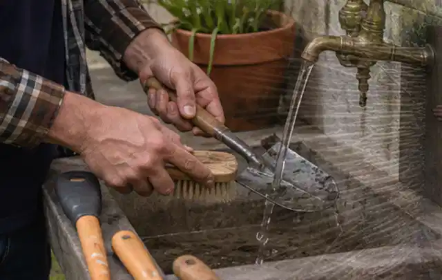 Hände reinigen gebrauchte Gartengeräte mit Bürste und Wasser am Außenbecken; Thema Komposter, Schwerpunkt Fehlerhilfe; Ergebnis.