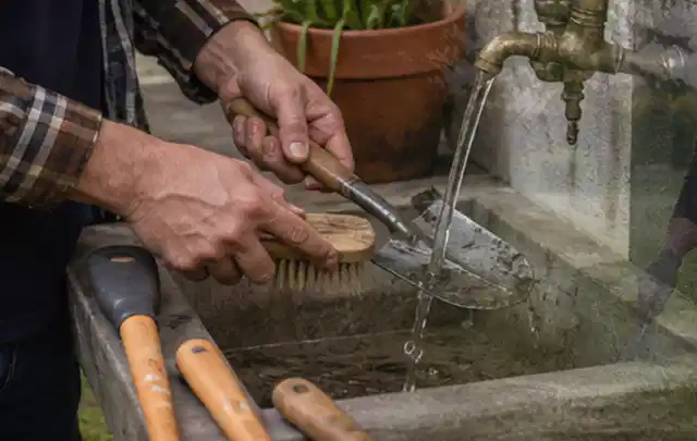 Hände reinigen gebrauchte Gartengeräte mit Bürste und Wasser am Außenbecken; Thema Komposter, Schwerpunkt Gärten mit kleiner Fläche; Kontrolle.