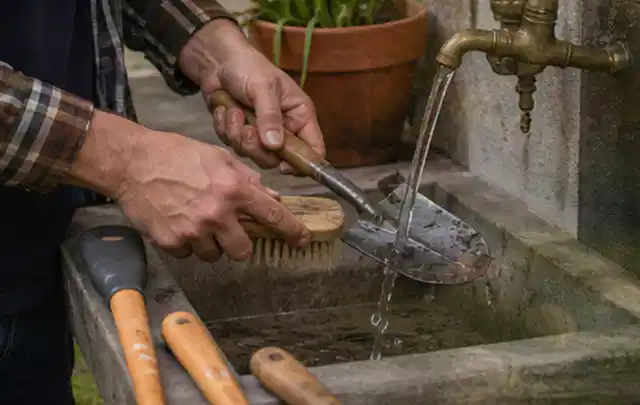 Hände reinigen gebrauchte Gartengeräte mit Bürste und Wasser am Außenbecken; Thema Komposter, Schwerpunkt Nachhaltigkeit; Umsetzung.