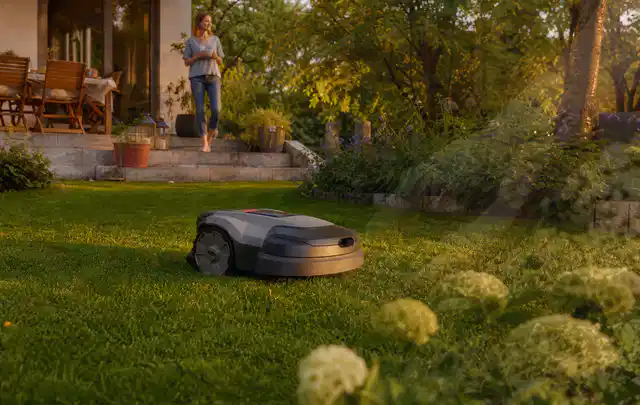 Mähroboter fährt am Abend über einen Rasen im Familiengarten; Thema Kress Mission, Schwerpunkt Anwendung; Kontrolle.