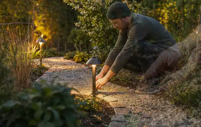 Person richtet eine niedrige warm leuchtende Gartenlampe am Kiesweg aus; Thema Kress Mission, Schwerpunkt Fehlerhilfe; Ausgangslage.