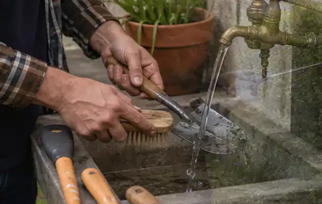 Hände reinigen gebrauchte Gartengeräte mit Bürste und Wasser am Außenbecken; Thema Kress Mission, Schwerpunkt Fehlerhilfe; Praxisalltag.