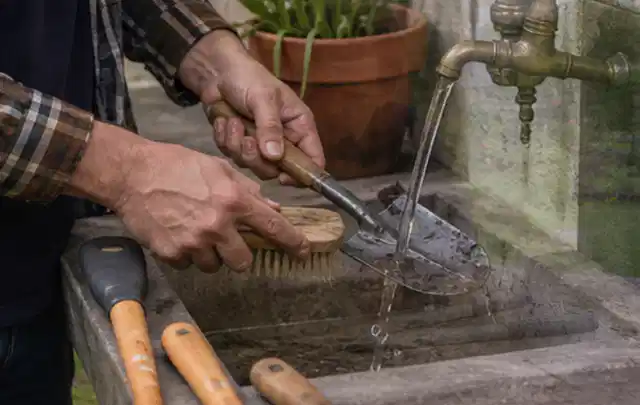 Hände reinigen gebrauchte Gartengeräte mit Bürste und Wasser am Außenbecken; Thema Kress Mission, Schwerpunkt Gärten mit großer Fläche; Umsetzung.