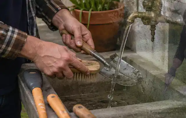 Hände reinigen gebrauchte Gartengeräte mit Bürste und Wasser am Außenbecken; Thema Kress Mission, Schwerpunkt Leistung; Kontrolle.