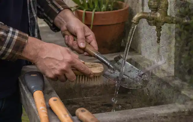 Hände reinigen gebrauchte Gartengeräte mit Bürste und Wasser am Außenbecken; Thema Kress Mission, Schwerpunkt Vergleich; Praxisalltag.