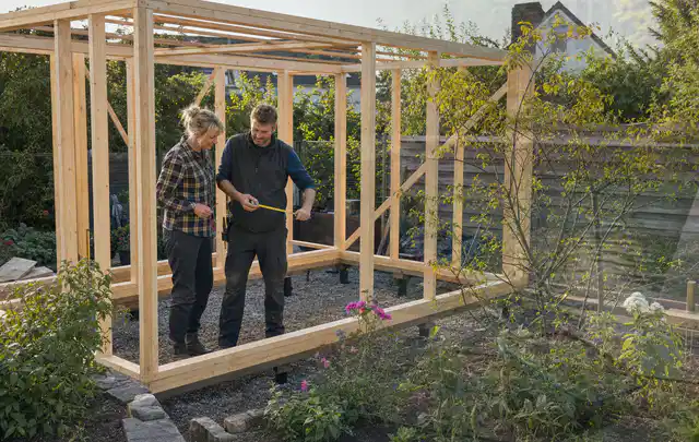 Person plant den Bau eines Gartenhauses auf einer vorbereiteten Fläche; Thema Lagerhaus im Garten, Schwerpunkt Standort; Praxisalltag.