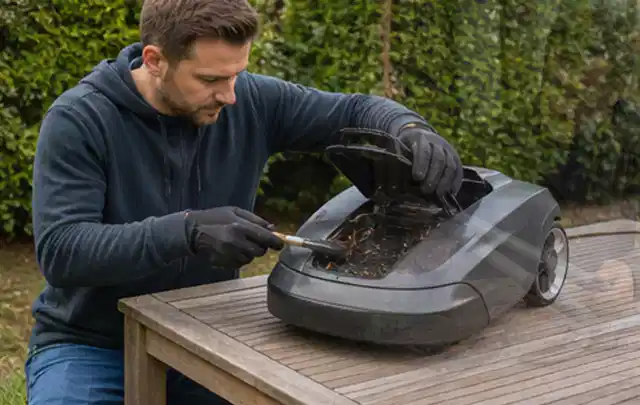 Person wartet einen geöffneten Mähroboter auf einem stabilen Gartentisch; Thema Laubbläser, Schwerpunkt Fehlerhilfe; Kontrolle.