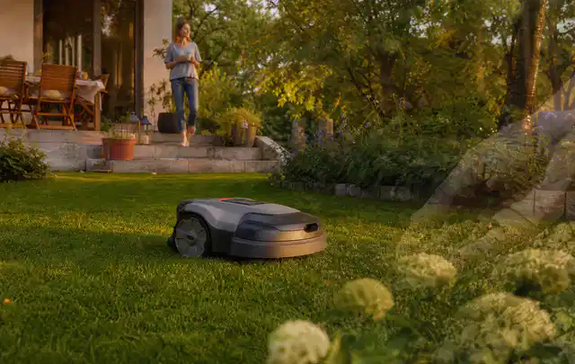 Mähroboter fährt am Abend über einen Rasen im Familiengarten; Thema Mähroboter Akkus, Schwerpunkt Checkliste; Kontrolle.
