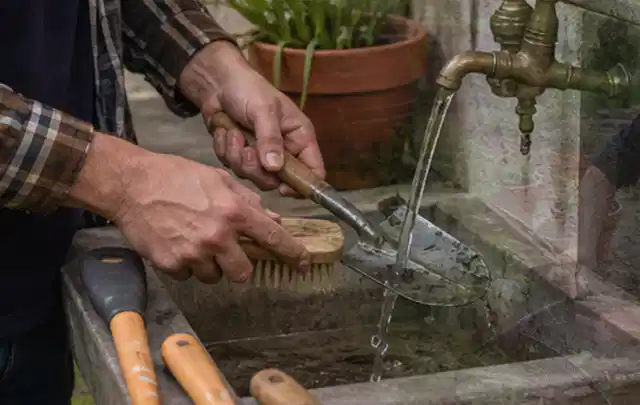 Hände reinigen gebrauchte Gartengeräte mit Bürste und Wasser am Außenbecken; Thema Mähroboter Akkus, Schwerpunkt Leistung; Kontrolle.
