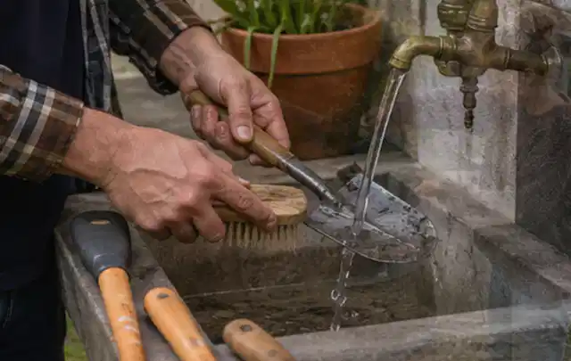 Hände reinigen gebrauchte Gartengeräte mit Bürste und Wasser am Außenbecken; Thema Mähroboter für große Gärten, Schwerpunkt Fehlerhilfe; Ausgangslage.