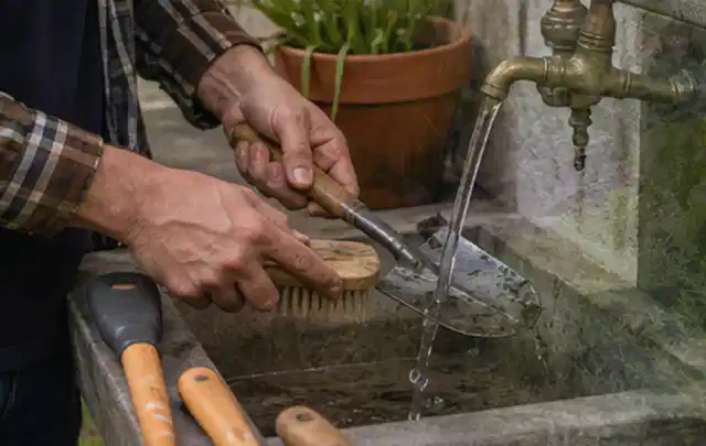 Hände reinigen gebrauchte Gartengeräte mit Bürste und Wasser am Außenbecken; Thema Mähroboter für große Gärten, Schwerpunkt Reparatur; Ergebnis.
