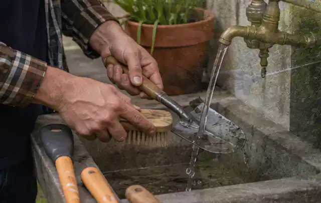 Hände reinigen gebrauchte Gartengeräte mit Bürste und Wasser am Außenbecken; Thema Mähroboter für Hanglagen, Schwerpunkt Ersatzteile; Ausgangslage.