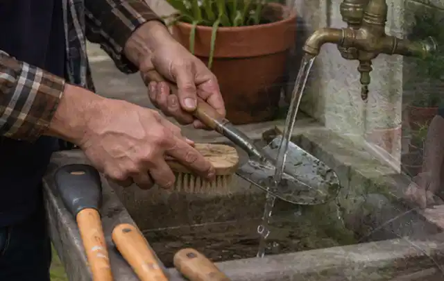 Hände reinigen gebrauchte Gartengeräte mit Bürste und Wasser am Außenbecken; Thema Mähroboter für Hanglagen, Schwerpunkt Mähroboter; Kontrolle.