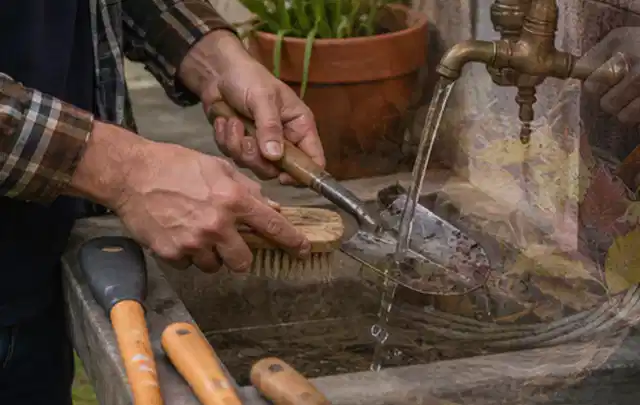 Hände reinigen gebrauchte Gartengeräte mit Bürste und Wasser am Außenbecken; Thema Mähroboter für Hanglagen, Schwerpunkt Nachhaltigkeit; Ergebnis.