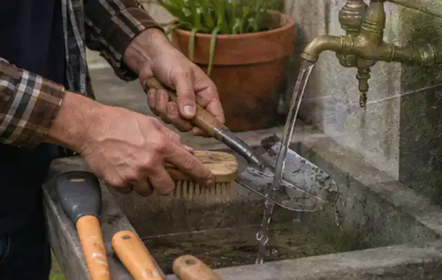 Hände reinigen gebrauchte Gartengeräte mit Bürste und Wasser am Außenbecken; Thema Mähroboter für Hanglagen, Schwerpunkt Sicherheit; Umsetzung.