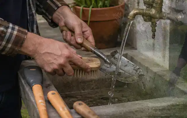 Hände reinigen gebrauchte Gartengeräte mit Bürste und Wasser am Außenbecken; Thema Mähroboter für Hanglagen, Schwerpunkt Testkriterien; Kontrolle.