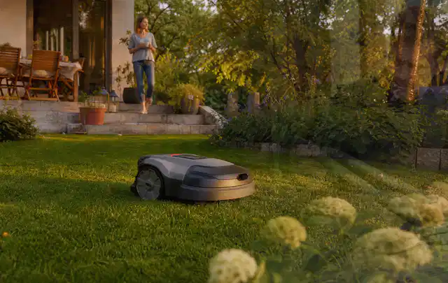 Mähroboter fährt am Abend über einen Rasen im Familiengarten; Thema Mähroboter für kleine Gärten, Schwerpunkt Dimensionierung; Umsetzung.