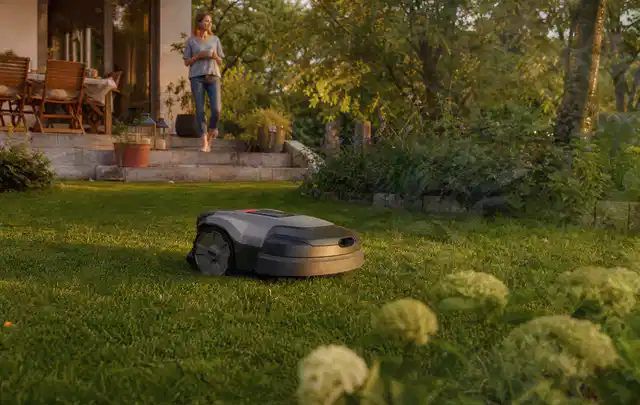 Mähroboter fährt am Abend über einen Rasen im Familiengarten; Thema Mähroboter für kleine Gärten, Schwerpunkt Vergleich; Umsetzung.