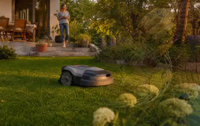 Mähroboter fährt am Abend über einen Rasen im Familiengarten; Thema Mähroboter Garagen, Schwerpunkt Checkliste; Ausgangslage.