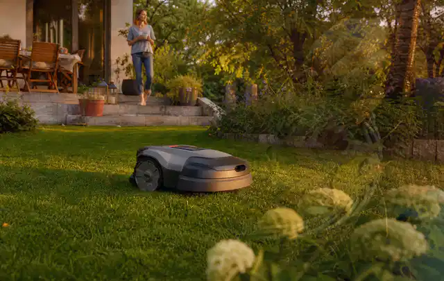 Mähroboter fährt am Abend über einen Rasen im Familiengarten; Thema Mähroboter Garagen, Schwerpunkt Testkriterien; Kontrolle.