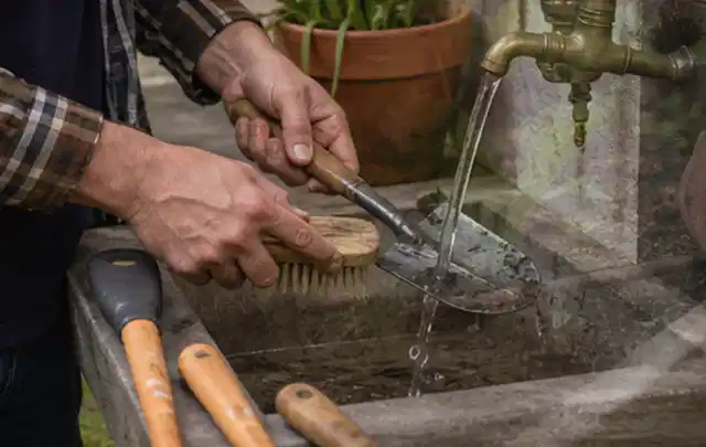 Hände reinigen gebrauchte Gartengeräte mit Bürste und Wasser am Außenbecken; Thema Mähroboter Installation, Schwerpunkt Testkriterien; Ausgangslage.
