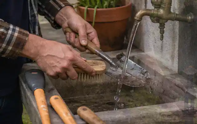Hände reinigen gebrauchte Gartengeräte mit Bürste und Wasser am Außenbecken; Thema Mähroboter Installation, Schwerpunkt Vergleich; Kontrolle.