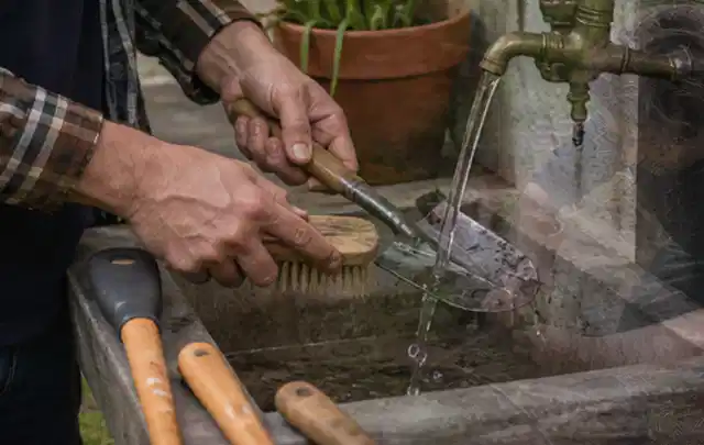Hände reinigen gebrauchte Gartengeräte mit Bürste und Wasser am Außenbecken; Thema Mähroboter Messer, Schwerpunkt Anwendung; Kontrolle.