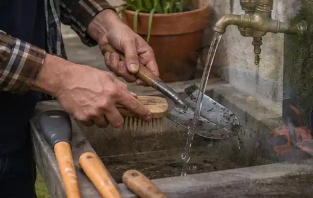 Hände reinigen gebrauchte Gartengeräte mit Bürste und Wasser am Außenbecken; Thema Mähroboter Messer, Schwerpunkt Checkliste; Praxisalltag.