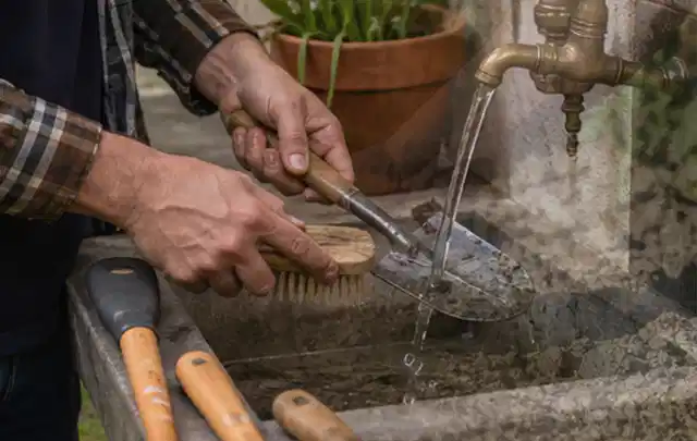 Hände reinigen gebrauchte Gartengeräte mit Bürste und Wasser am Außenbecken; Thema Mähroboter Messer, Schwerpunkt Ersatzteile; Ergebnis.