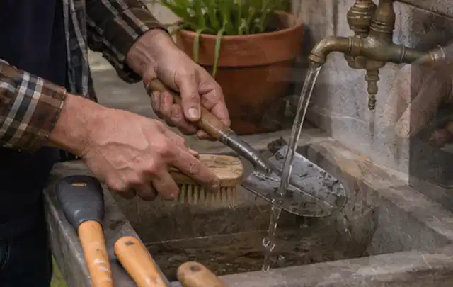 Hände reinigen gebrauchte Gartengeräte mit Bürste und Wasser am Außenbecken; Thema Mähroboter Messer, Schwerpunkt Fehlerhilfe; Ausgangslage.