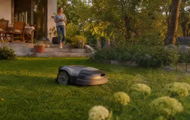 Mähroboter fährt am Abend über einen Rasen im Familiengarten; Thema Mähroboter mit GPS, Schwerpunkt Checkliste; Praxisalltag.