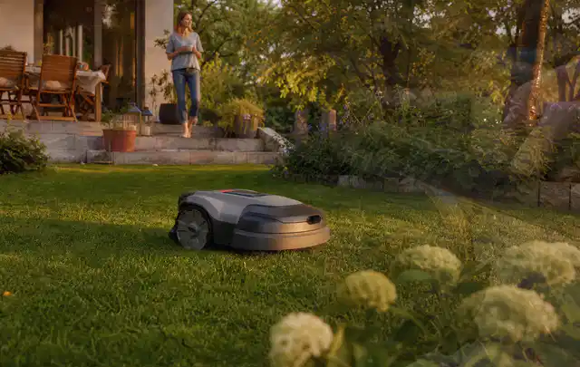 Mähroboter fährt am Abend über einen Rasen im Familiengarten; Thema Mähroboter mit GPS, Schwerpunkt Testkriterien; Praxisalltag.