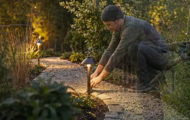 Person richtet eine niedrige warm leuchtende Gartenlampe am Kiesweg aus; Thema Mammotion Luba, Schwerpunkt Checkliste; Umsetzung.