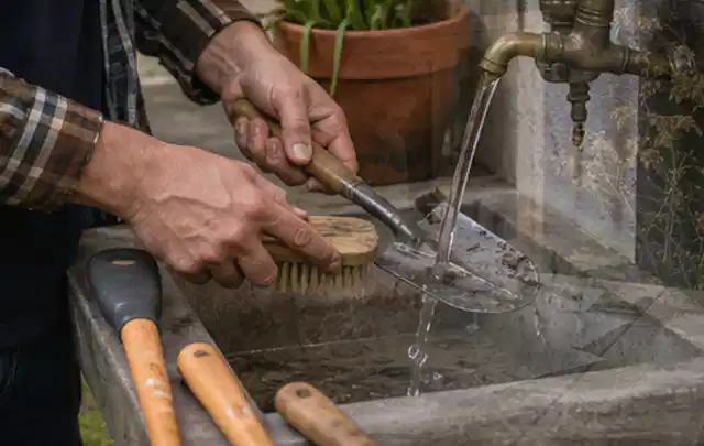 Hände reinigen gebrauchte Gartengeräte mit Bürste und Wasser am Außenbecken; Thema Mammotion Luba, Schwerpunkt Dimensionierung; Ausgangslage.
