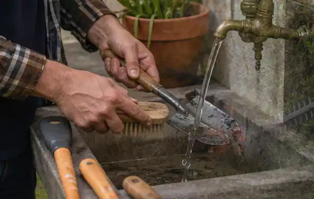 Hände reinigen gebrauchte Gartengeräte mit Bürste und Wasser am Außenbecken; Thema Mammotion Luba, Schwerpunkt Mähroboter; Ergebnis.