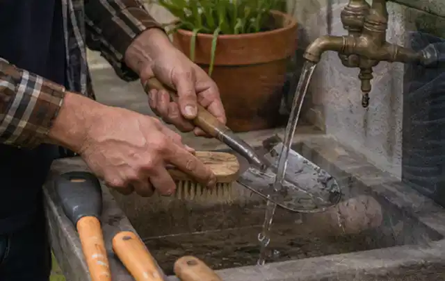 Hände reinigen gebrauchte Gartengeräte mit Bürste und Wasser am Außenbecken; Thema Mammotion Luba, Schwerpunkt Winterlager; Ergebnis.