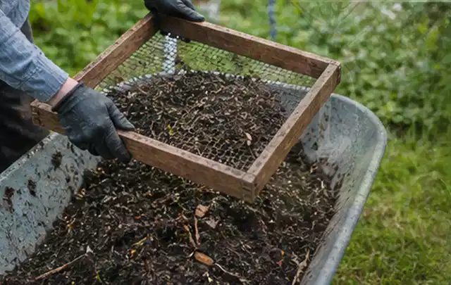 Behandschuhte Hände sieben reifen Kompost über einer Gartenschubkarre; Thema Mini Gewächshaus, Schwerpunkt Checkliste; Ausgangslage.