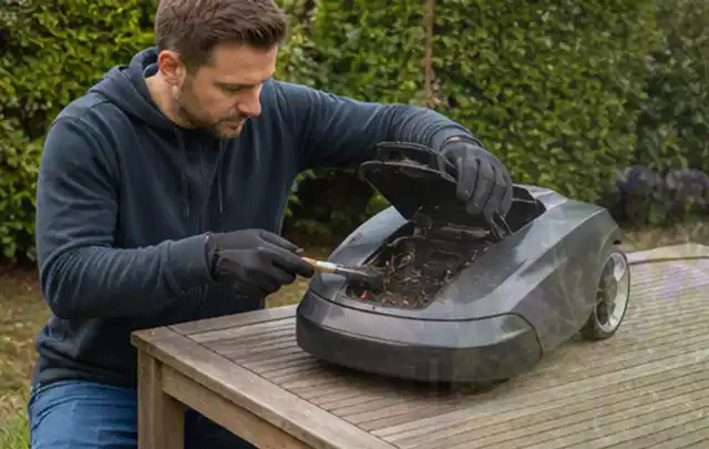 Person wartet einen geöffneten Mähroboter auf einem stabilen Gartentisch; Thema Motorhacken, Schwerpunkt Wartung; Umsetzung.