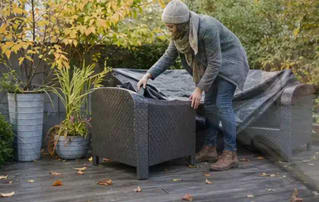 Person deckt Gartenmöbel vor der kalten Jahreszeit sorgfältig ab; Thema Outdoor Küchen, Schwerpunkt Anwendung; Umsetzung.