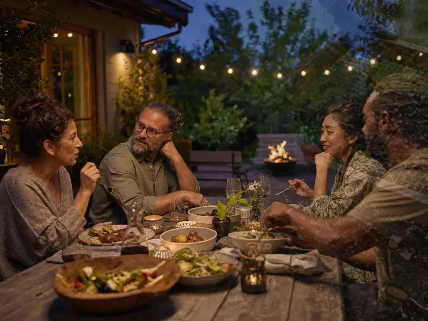 Menschen verbringen einen ruhigen Abend an einem Sitzplatz im Garten; Thema Outdoor Küchen, Schwerpunkt Dimensionierung; Titelbild.