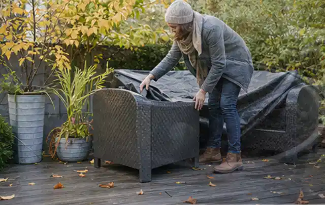 Person deckt Gartenmöbel vor der kalten Jahreszeit sorgfältig ab; Thema Outdoor Küchen, Schwerpunkt Dimensionierung; Umsetzung.